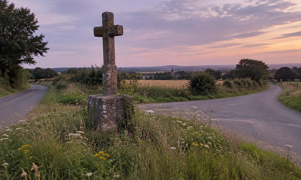 La croix du carrefour dans le pré, entre deux routes de campagne, au moment où le ciel se rend.